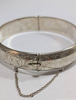 Silver bangle bracelet shown from a side angle highlighting the clasp and safety chain.