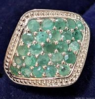 Close-up front view of the emerald stones on the ring, showing the multiple small round green emeralds set close together in a silver beaded border.