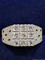 Close-up front view of silver ring with nine clear stones arranged in a 3x3 pattern, showing textured finish and cutout details on the band.