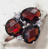 Close-up front view of the sterling silver ring with three faceted garnet stones and four small clear stones.