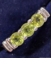 Close-up top view of sterling silver ring with three faceted peridot stones showing color and setting detail.
