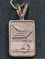 Front view of the silver rectangular pendant showing stylized wing and number 25 design on textured background.
