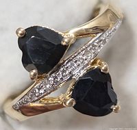 Close-up image showing front and top view of ring with two heart-shaped dark blue sapphire stones and accent stones set in sterling silver.