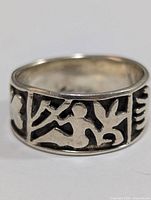 Front view showing detailed tribal style human and animal figures carved in silver with dark oxidized background.