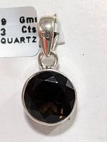 Close-up of front of round faceted smokey quartz gemstone pendant set in 925 silver showing the 925 mark on the bail and the stone's color and cut.