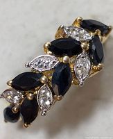 Close-up of ring front showing dark blue marquise-shaped sapphire stones and clear accent stones in gold prongs.