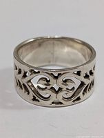 Close-up image of silver ring showing detailed filigree heart and leaf pattern on band.