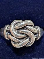 Close-up image of a sterling silver ring displaying a rounded knot design on a dark fabric background.