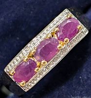 Close-up image showing the three oval rubies set in gold prongs on a detailed silver band