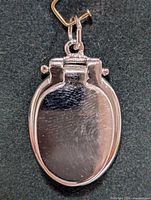 Front view of the oval silver pendant with smooth reflective surface against black background.