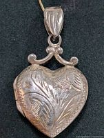Front and angle views showing the detailed engraving on the heart-shaped silver locket pendant.