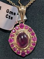 Close-up of the pendant showing the central oval cabochon ruby surrounded by smaller faceted rubies, attached to a silver chain.