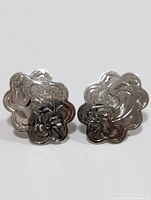 Front view of the pair of silver earrings shaped like flowers with engraved patterns.