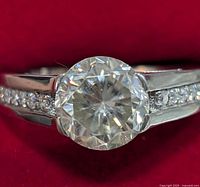 Front view showing round center moissanite stone and flanking pavé stones on band.