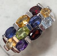 Close-up of silver band ring showing double row of multicolor oval gemstones with a variety of colors including blue, yellow, red, green, purple, and light blue.