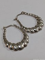 Side angled close-up showing twisted, rounded silver hoop earrings with latch back closure.
