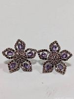 Front view of the flower-shaped silver earrings with purple amethyst stones in each petal and detailed center