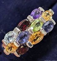 Close-up photo showing the front view of the ring with nine oval multi-color gemstones visible in alternating colors and hues.