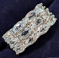 Close-up image of a sterling silver ring with three rows of light blue oval blue topaz gemstones securely set in prongs.