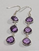 Front-facing photo of both amethyst dangle earrings showing three faceted purple stones each set in sterling silver and hook clasps.