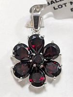 Front view of silver flower pendant with six pear-shaped garnets and one round garnet in the center.