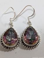 Pair of silver earrings with teardrop mystic topaz stones laying flat on white background showing front detail and intricate silver setting.