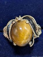 Close-up front view of ring showing oval Tiger Eye stone set in detailed silver claw setting