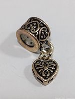 Close-up photo of a silver Pandora style bead with intricate heart designs and attached dangling heart charm.