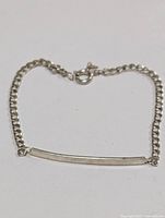 7-inch silver chain bracelet displayed fully extended, showing curved rectangular bar and lobster clasp.