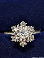 Top view of sterling silver ring with clear cubic zirconia stones arranged in a flower shape on a dark blue fabric background.