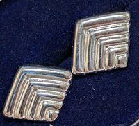 Close-up side-by-side photo of two silver geometric stud earrings showing the stepped chevron design.