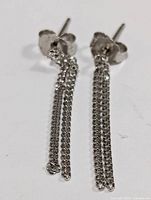 Close-up of one silver dangle earring showing stud post and small interlinked chain tassels.