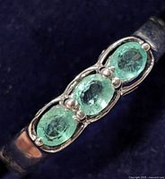 Close-up view of the three oval-shaped translucent green emerald stones mounted on silver ring.