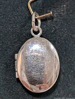 Close-up image of the front side of the oval silver locket pendant showing the textured surface and attachment loop.