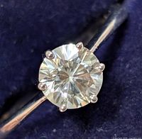 Close-up image of the silver ring showing the round faceted moissanite stone held by six prongs.