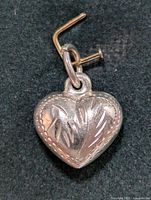 Close-up front view of the silver heart-shaped pendant showing engraved feather designs and beaded edging.
