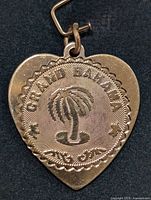 Front view of silver heart-shaped pendant with 'Grand Bahama' text and palm tree design on textured medallion.