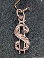 Close-up front view of small silver dollar sign pendant showing textured design and attachment loop.