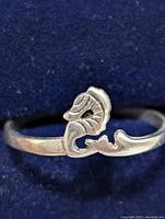 Close-up photo of silver ring showing seahorse design on a blue background.