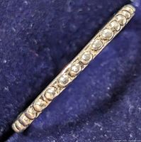 Close-up side view of a thin silver ring with clear round stones set around it showing detailing and texture of the band and stones.
