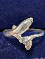 Close-up photo of silver whale tail ring on dark blue background showing detailed whale tail design and polished surface.