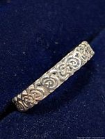 Close-up photo of silver ring showing intricate Celtic knot pattern on band, side view on dark background.
