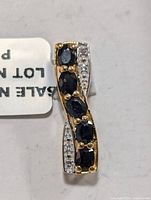 Front and angled front view of a rectangular gold-tone pendant with 5 oval dark blue sapphires and rows of small clear stones on each side.