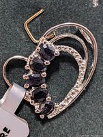 Close-up of silver heart-shaped pendant with dark sapphire stones and small clear stone accents.