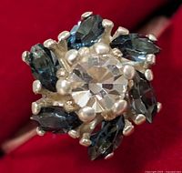 Close-up of the silver ring showing the clear central stone and surrounding dark blue marquise-shaped sapphire stones in a cluster floral design.