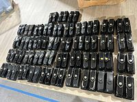 Overview of all 43 black leather pouches with flap and snap button closures laid out on a table.