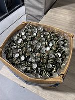 Photo of a large cardboard box filled with silver metal bottle caps, showing the tops with A&W branding and ridged edges.