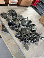 Photo showing an assortment of vintage pewter items including plates, pitchers, cups, a lidded tankard, a shell-shaped dish, and other vessels arranged on a wooden surface.