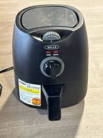 Front view of Bella black air fryer with temperature dial on top and control knob on front, stickers on handle.