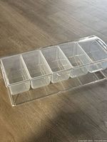 Top view of clear plastic serving tray with six removable condiment compartments on a wood floor.